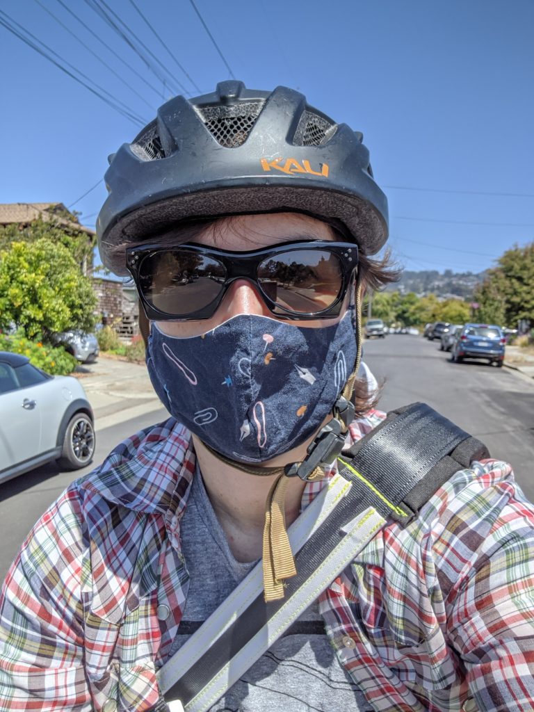 Selfie of me wearing a bike helmet, sunglasses, and mask in the middle of the street. 