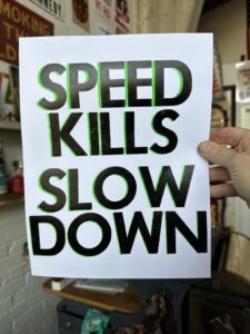 A poster saying "SPEED KILLS SLOW DOWN"