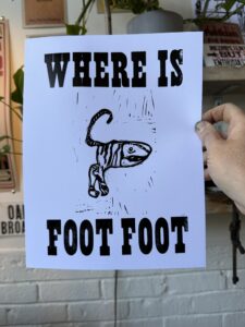 A hand holding a sign that says "where is foot foot" with a carved illustration of a tiger like creature in the middle.